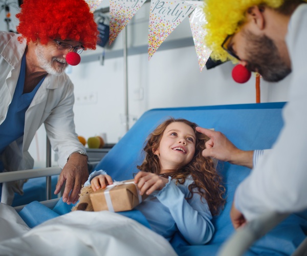 doctors dressed up as clowns with a young girl in hospital