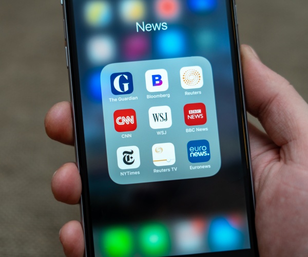 male hand holding black apple iphone with icons of news media