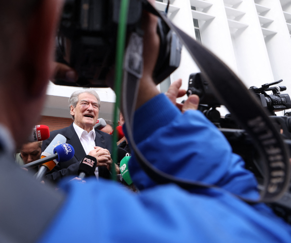 berisha talks to the press as he is framed by the arm of a camera operator