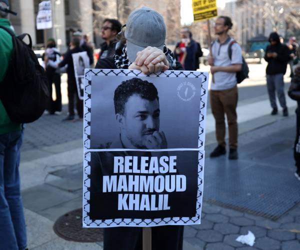 a person holds a release mahmoud khalil poster amid protesters on the street