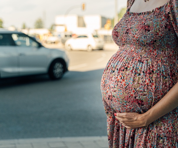 pregnant woman outside on city street next to a car