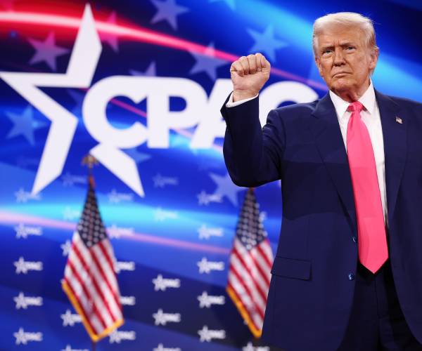 trump raises as fist as he stands in front of a cpac logo