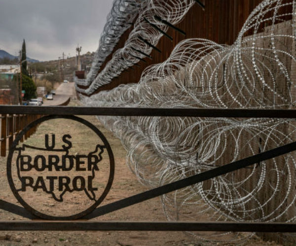 border fence with razor wire and the border patrol logo