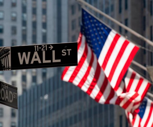 american flags behind a wall street street sign