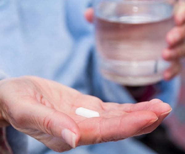 woman's hand holding a white pill, other hand holding a glass of water