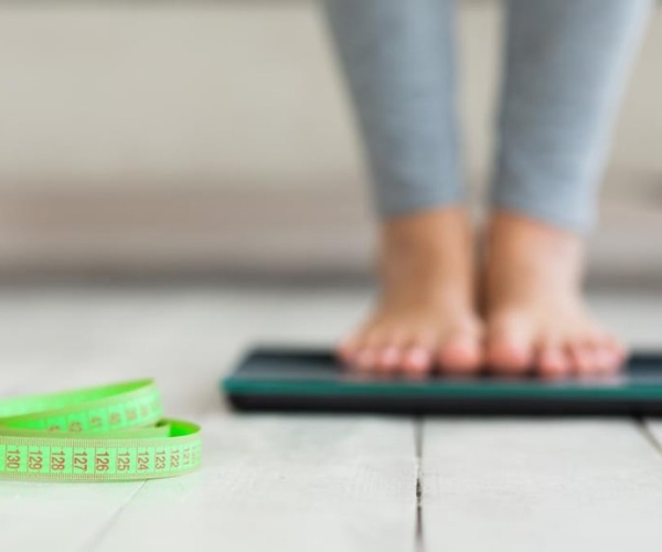 woman's feet on scale and measuring tape nearby