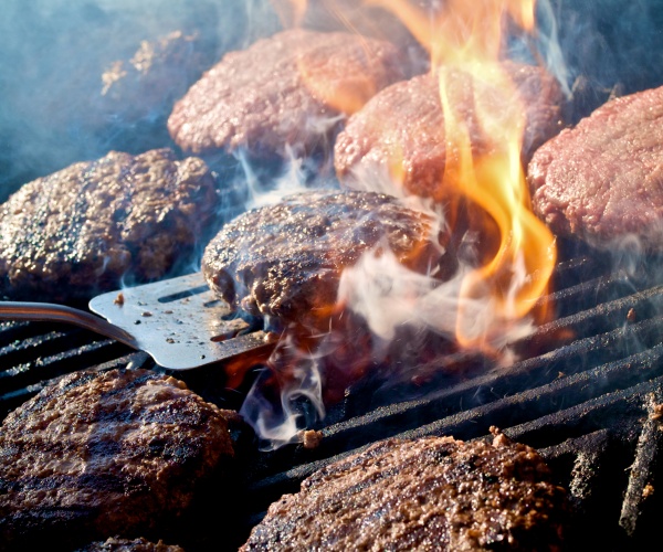 close up of grilling hamburgers over flame, with smoke