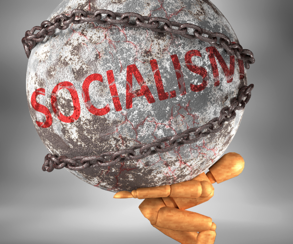 wooden man carrying boulder that says socialism and is wrapped in chains on his back