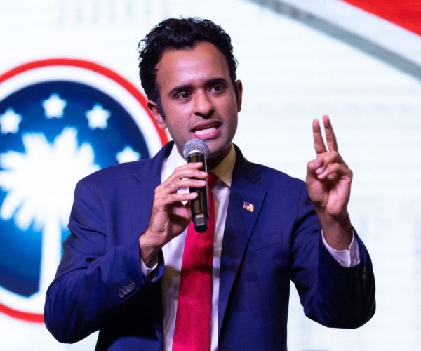 vivek ramaswamy in red tie and blue suit gestures with two fingers up