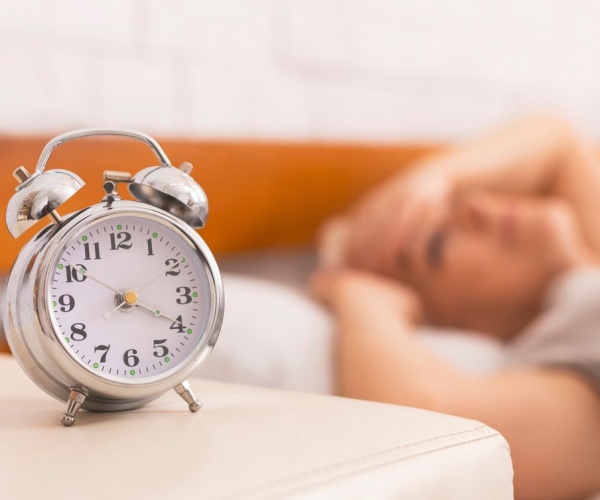 woman awake with hot flashes in the middle of the night, as shown on alarm clock on side of bed