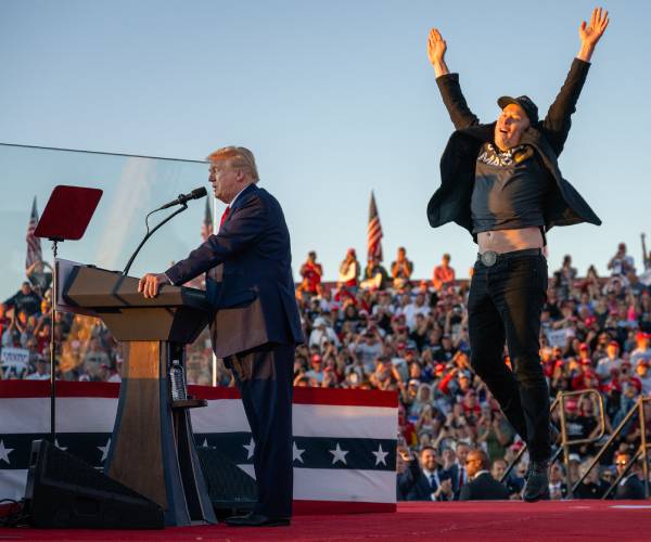 donald trump at the podium with elon musk standing behind him jumping up with arms raised