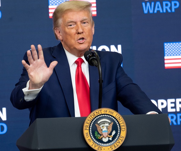 donald trump holds up hand while standing behind podium