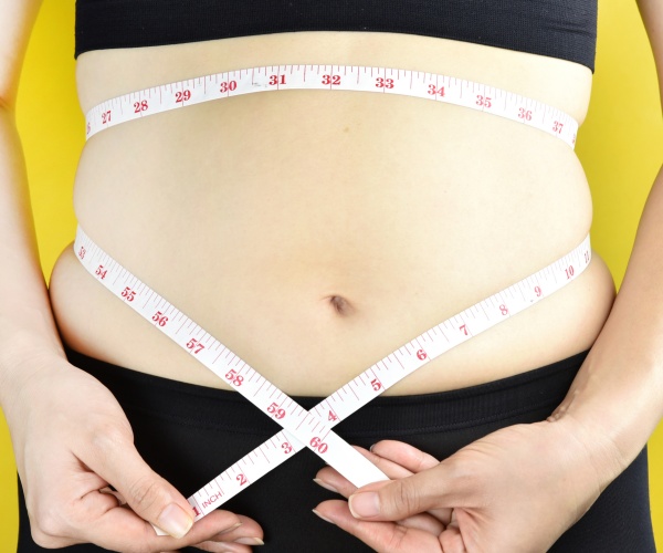 overweight woman with excess belly fat measuring waist