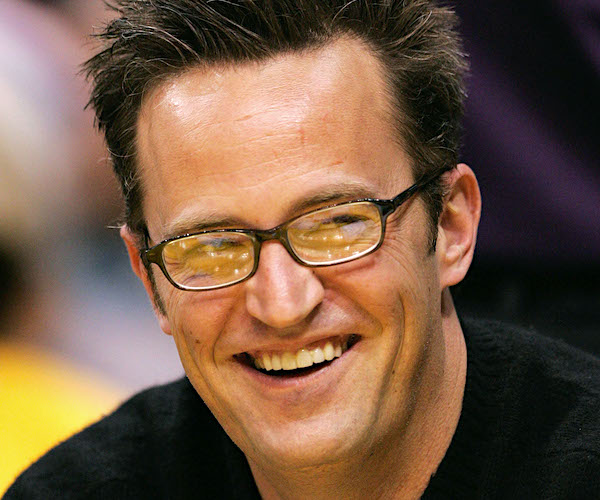 mathew perry wears yellow tinted glasses and spiked hair with a wide smile