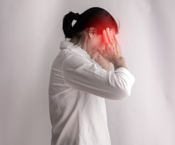 woman standing with hands on head in pain with headache