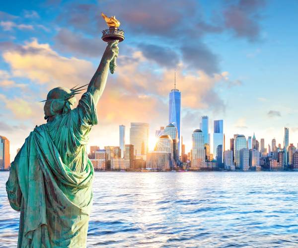 statue of liberty and new york city skyline at sunset