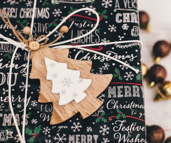 a wrapped christmas gift with a wooden cutout tree instead of a bow