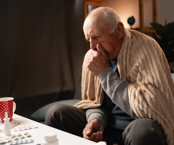 older man on couch with blanket, medicines, coughing with RSV or COVID