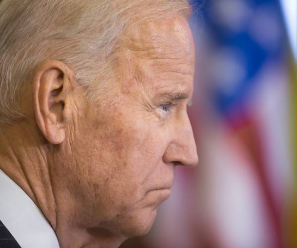 biden looking sad in front of an american flag