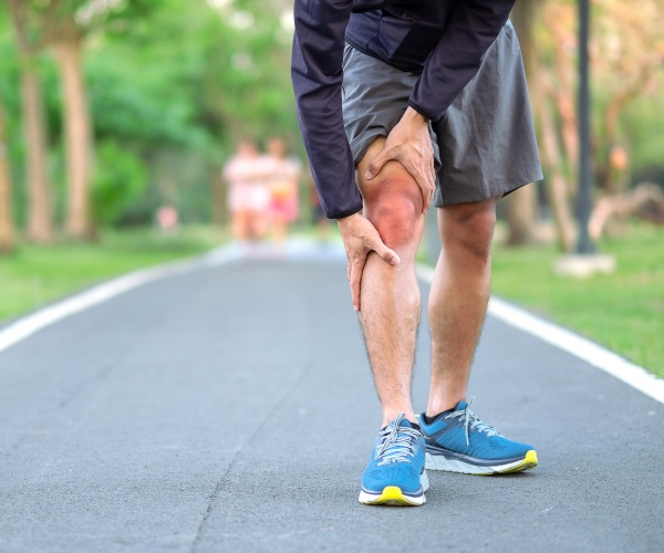 man in shorts out running holding knee in pain