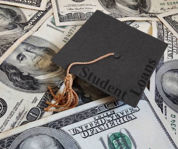 a graduation cap with the words student loan on top of a pile of hundreds