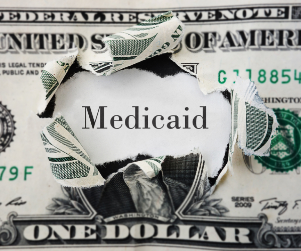 a dollar bill with the middle torn out and the word medicaid inside