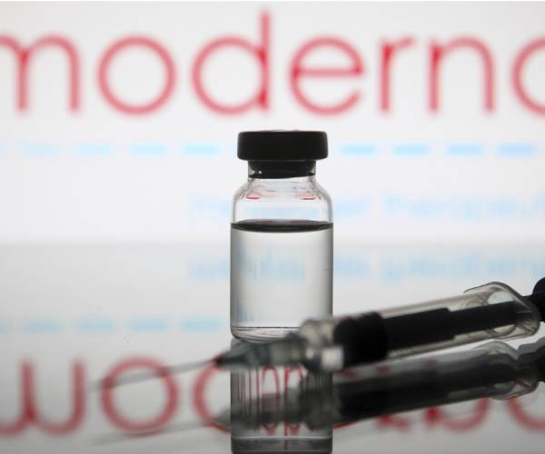 a vial an syringe in front of the moderna logo