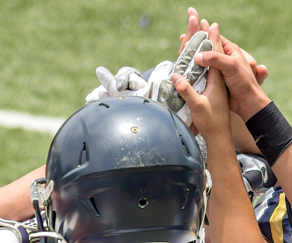 football players raise their hands together in a huddle