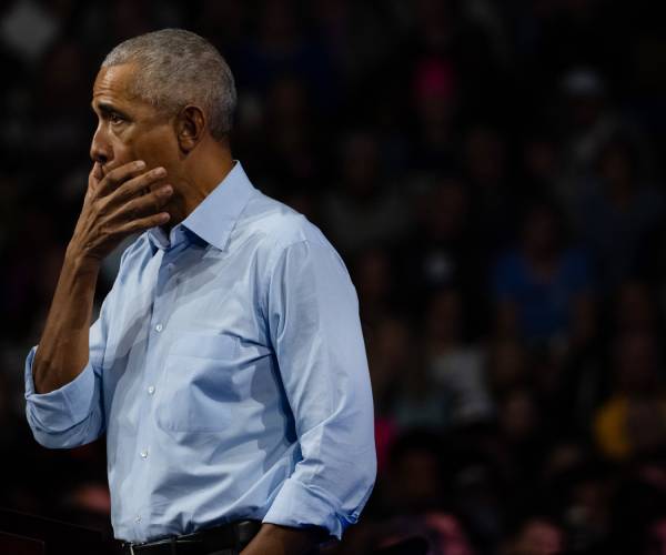 obama with his hand over his mouth facing out of the picture with a black background