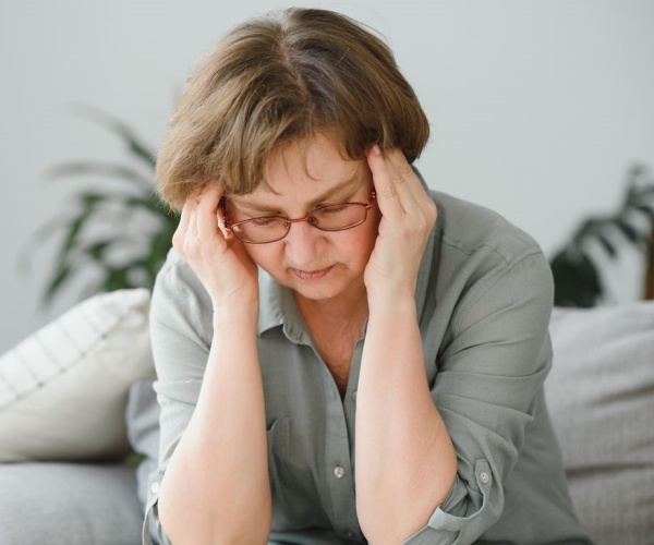 older woman looking stressed, holding head in hands while sitting on couch