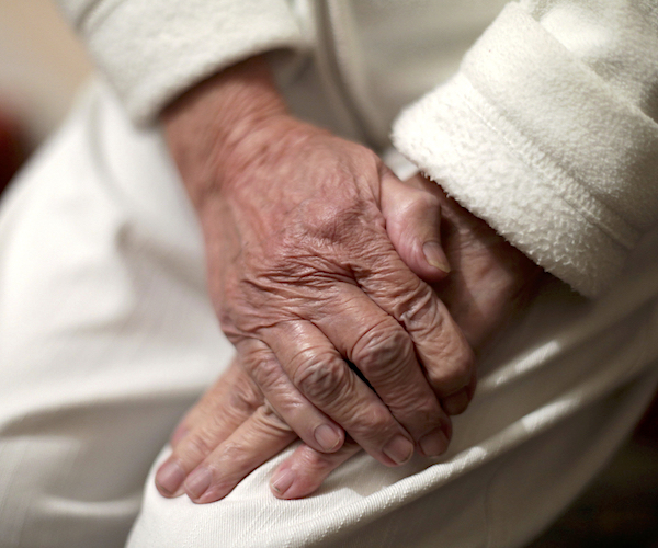 an elderly woman folds her weathered and wrinkled hands in her lap