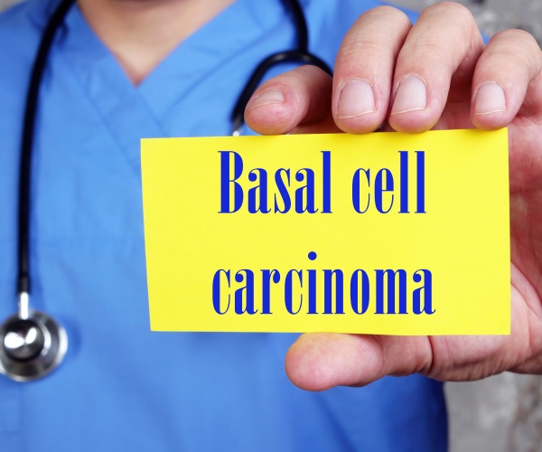 physician in scrubs holding up a small card that says "basal cell carcinoma"