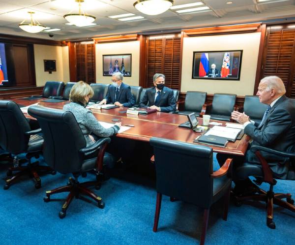 biden and staff at a table with putin on a video screen