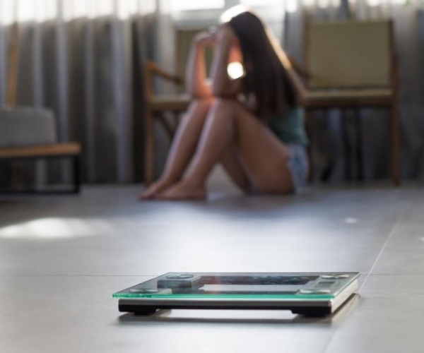 woman sitting in corner with head in hands, with scale on other side of room