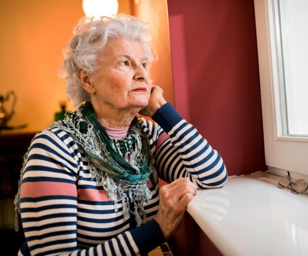 older woman looking out a window looking sad