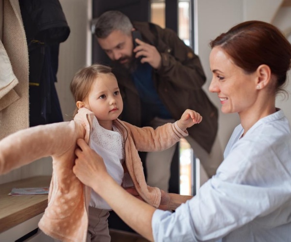 woman helping child put on coat, get out door to school