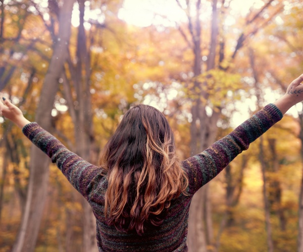 woman in woods with arms open to fall trees