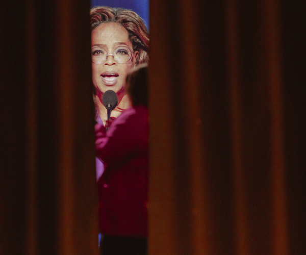 oprah winfrey on a giant television screen in the background seen between two curtains in the foreground